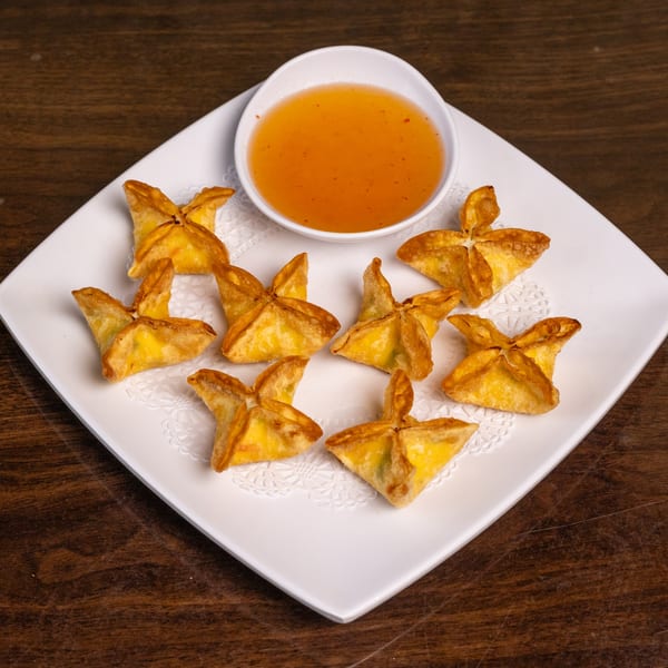 Crispy golden crab rangoons arranged on a white plate with a side of sweet chili dipping sauce.